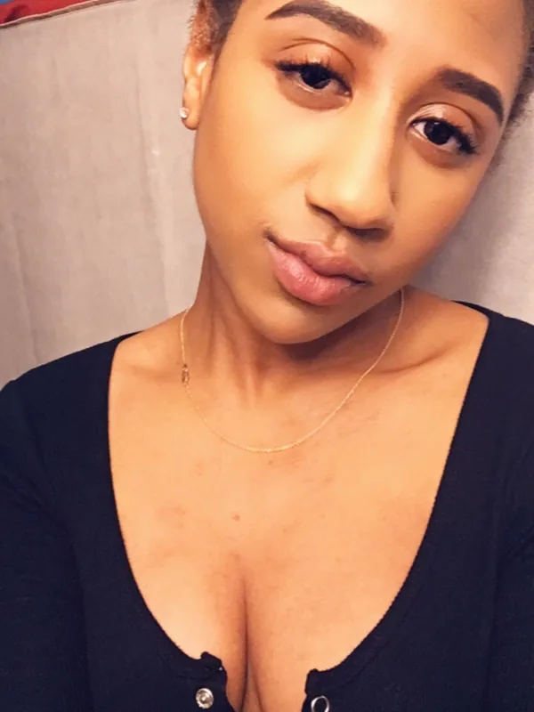 Portrait en gros plan d'une femme aux cheveux courts, portant un haut noir à col profond et un collier fin, regardant l'objectif.