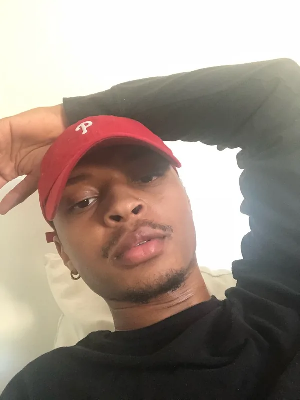 Portrait d'un homme portant une casquette rouge et un sweat-shirt noir, regardant l'objectif avec la main sur la tête.