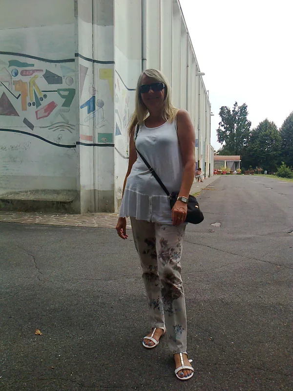 Femme blonde en tenue d'été posant devant un mur avec graffiti, portant lunettes de soleil et sac à bandoulière.