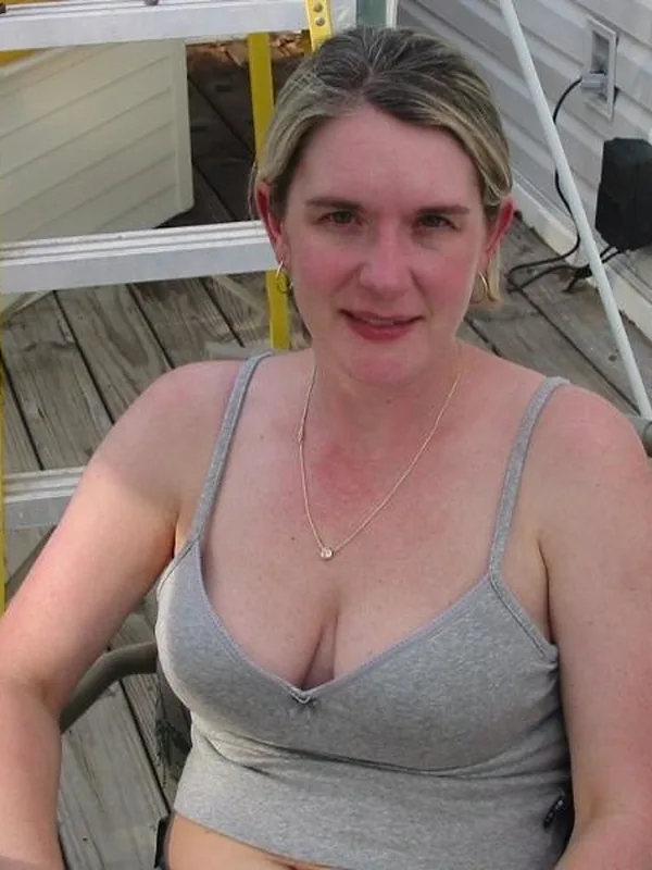Femme assise sur une chaise de jardin en terrasse, portant un haut gris, regardant l'objectif.
