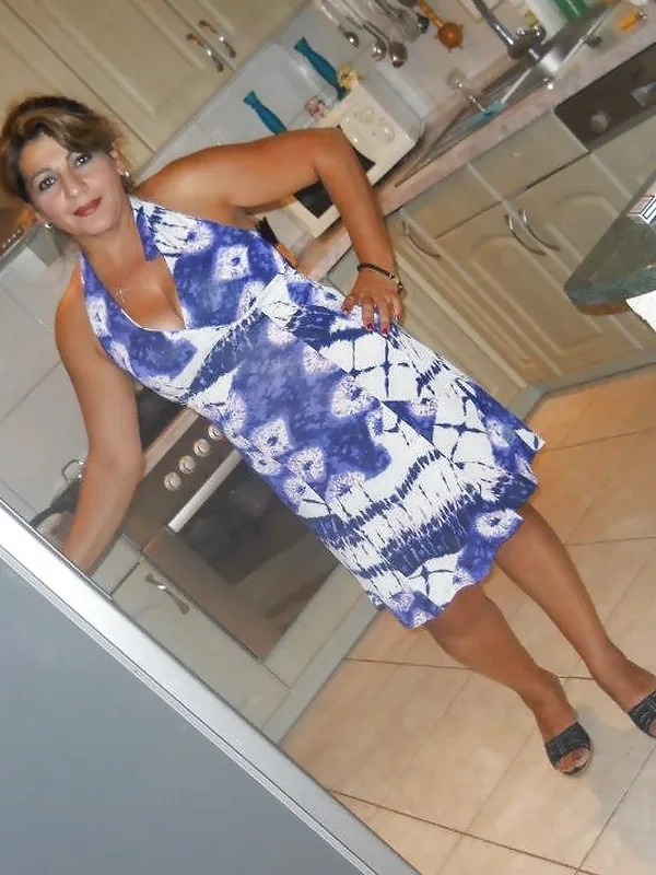 Femme en robe bleue et blanche posant dans une cuisine, regardant l'objectif, vue en contre-plongée.