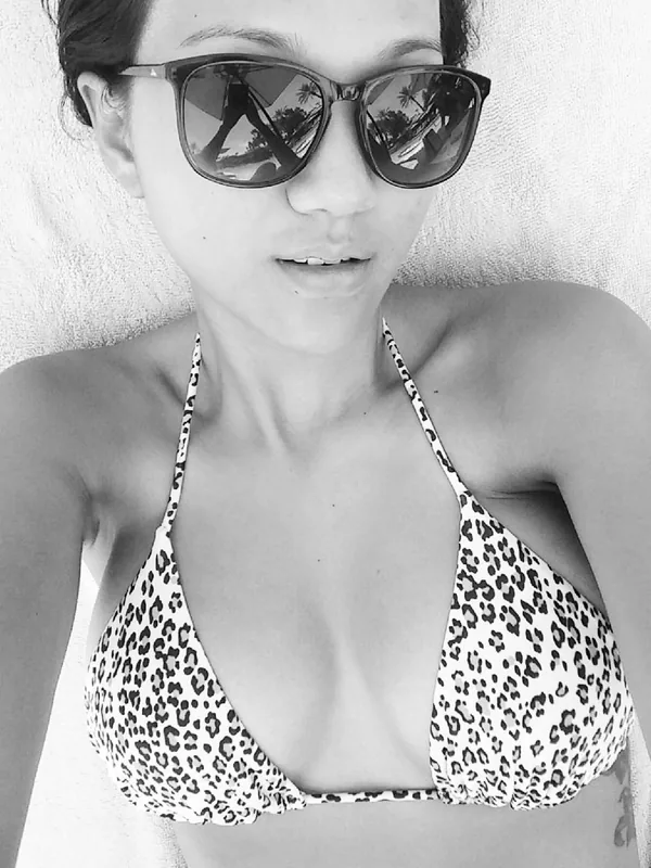 Portrait en noir et blanc d'une femme en haut de bikini léopard, portant des lunettes de soleil, allongée sur une serviette.