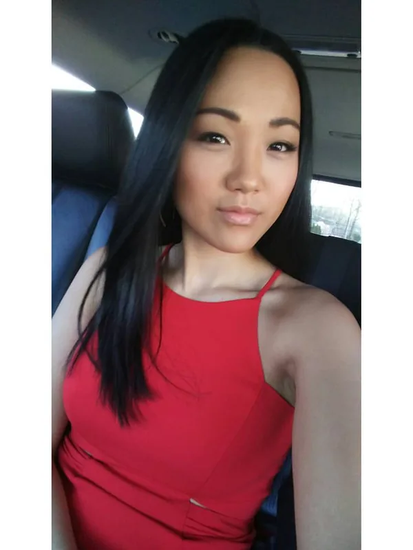 Portrait d'une femme aux cheveux noirs portant une robe rouge, assise dans une voiture, regardant l'objectif.