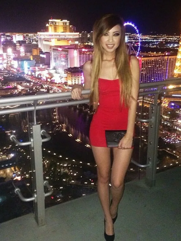 Femme en robe rouge posant sur une terrasse avec vue sur Las Vegas la nuit.