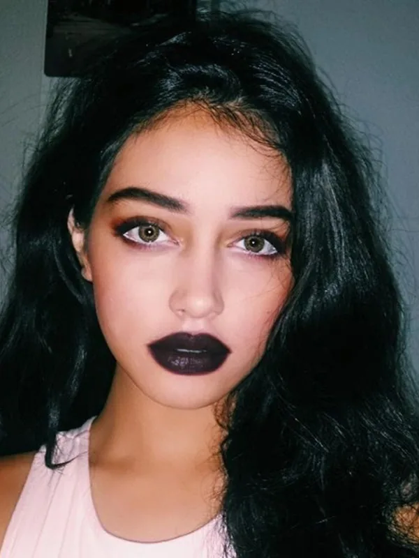 Portrait en gros plan d'une jeune femme aux cheveux noirs, maquillée avec du rouge à lèvres noir, portant un haut rose clair.