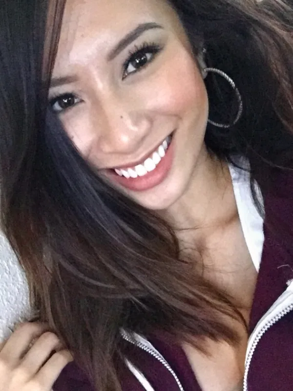 Portrait en gros plan d'une femme souriante aux cheveux foncés, portant une veste bordeaux et un haut blanc, regardant l'objectif.