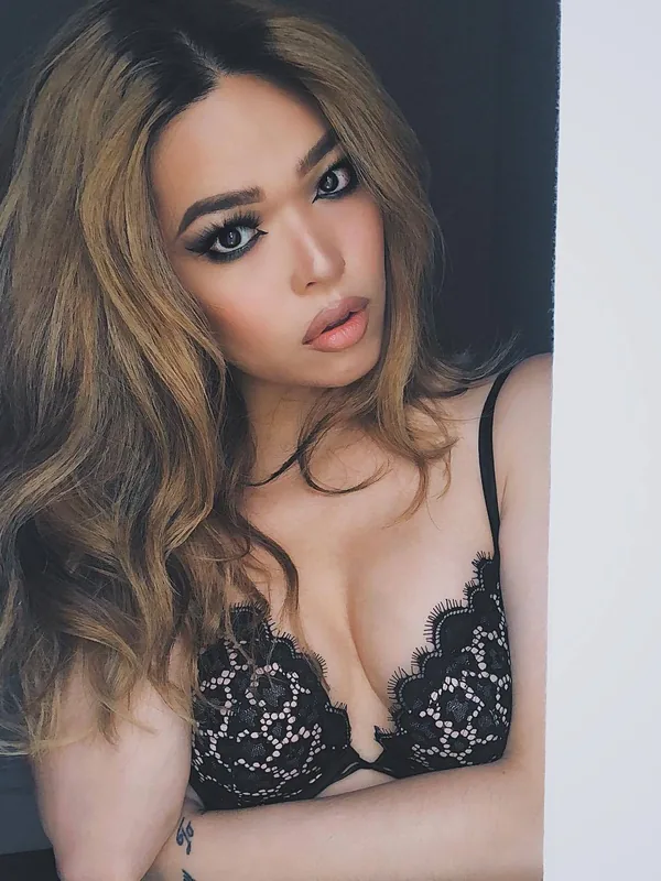 Portrait d'une femme aux cheveux ondulés portant un soutien-gorge noir en dentelle, regardant l'objectif.
