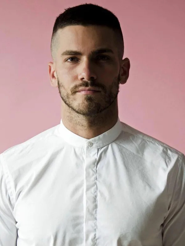 Portrait d'un homme en chemise blanche sur fond rose, regardant l'objectif.