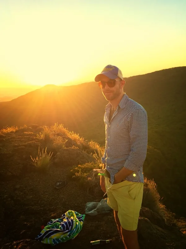Homme en tenue décontractée posant sur un sommet rocheux au coucher du soleil.
