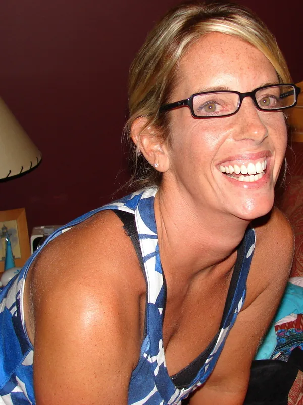Portrait d'une femme souriante portant des lunettes et un haut à motifs bleus et blancs, dans un cadre intérieur.